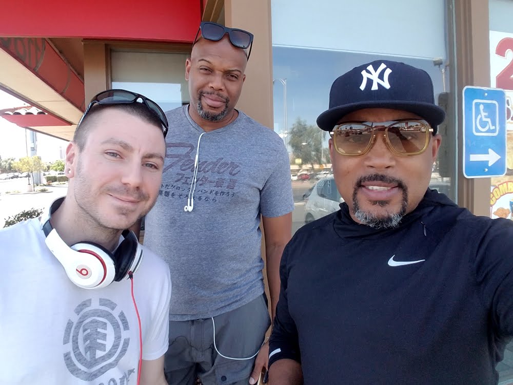Chance Trahan (left, white t-shirt with headphones) posing outdoors with Chauncey (center, gray t-shirt) and Daymond John (right, black hoodie and NY cap)